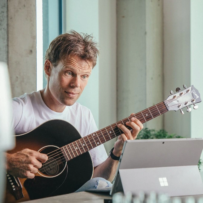 Jaap Kwakman met gitaar achter een laptop tijdens een online gitaarles